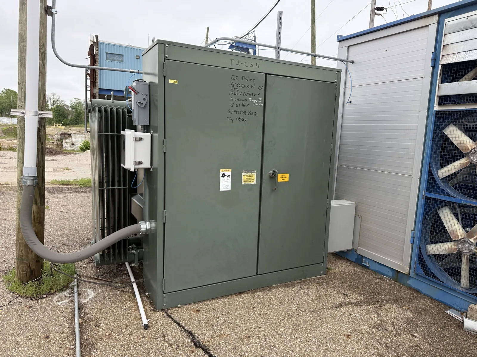 Green pad-mount transformer with radiator fins beside a plant building — Concord, CA